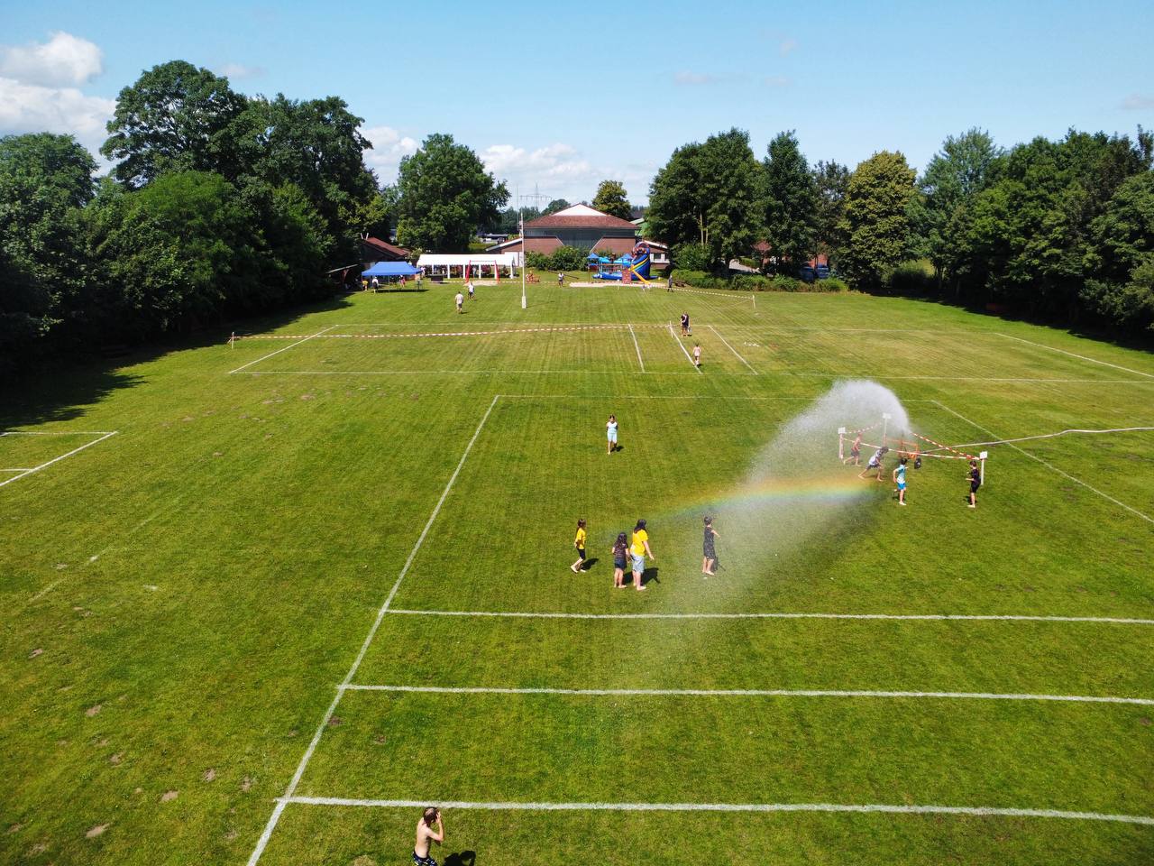 Abkühlung auf dem Sportplatz: Kinder laufen beim Kindervogelschießen durch den Rasensprenger.