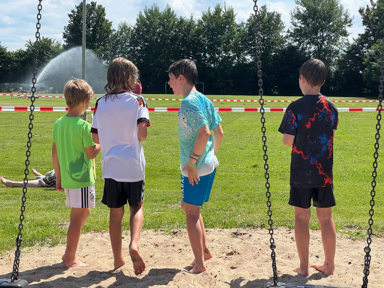 Sommerliche Abkühlung am Wasserstrahl auf dem Sportplatz.