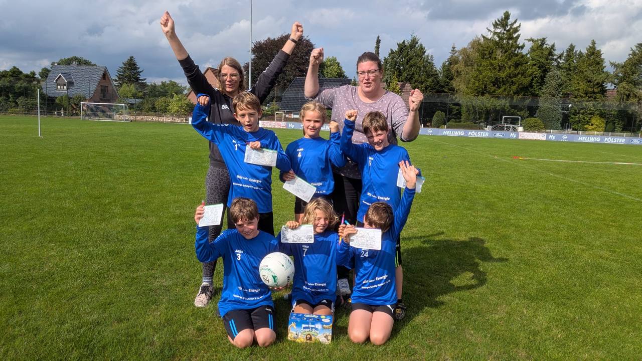 Jubelnde U10-Mannschaft des TSV Schülp mit hochgehaltenen Armen und selbst gestalteten Schildern auf dem Faustballfeld