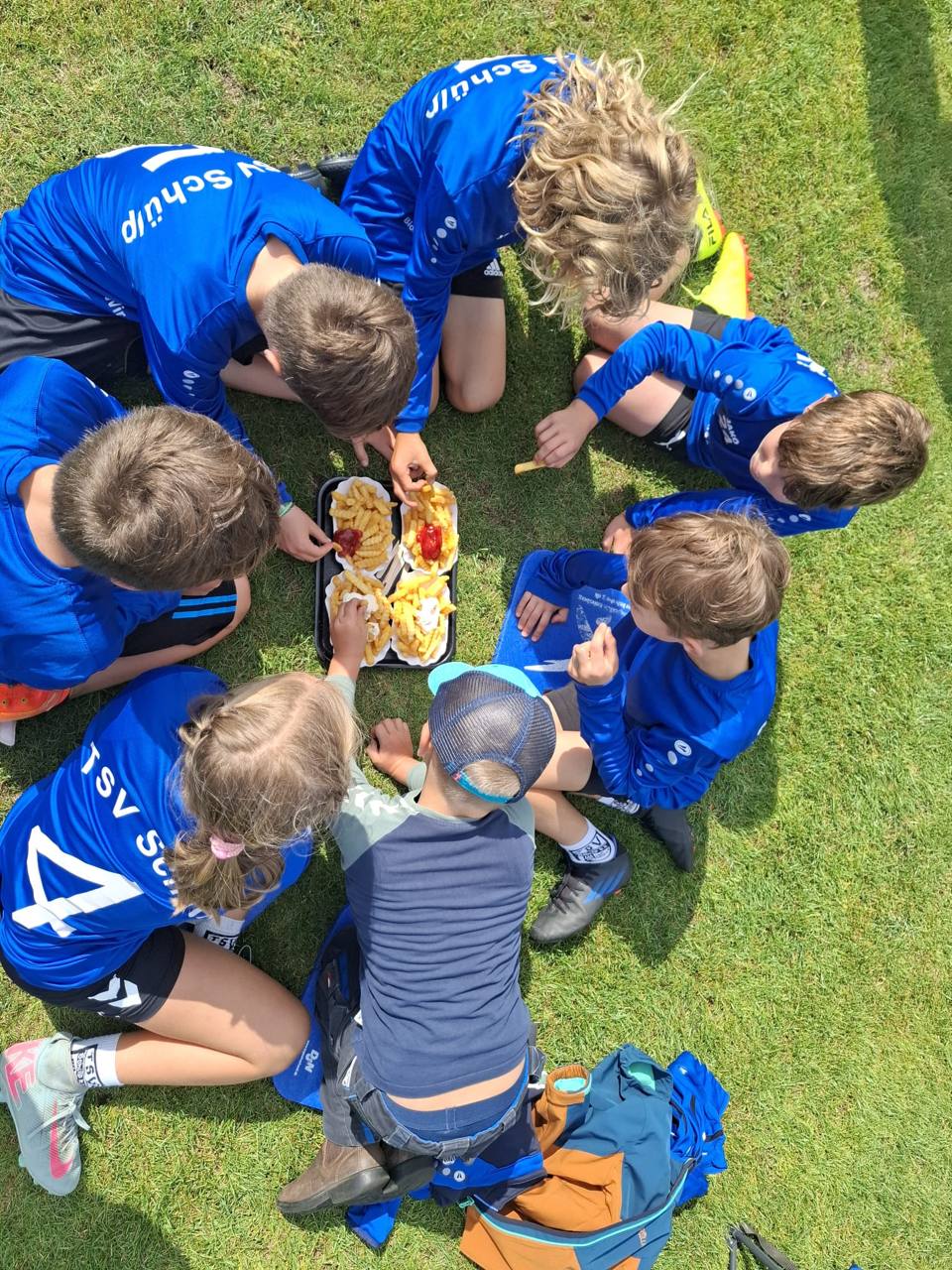Kinder der U10 des TSV Schülp sitzen nach dem Spiel gemeinsam mit Pommes auf dem Rasen