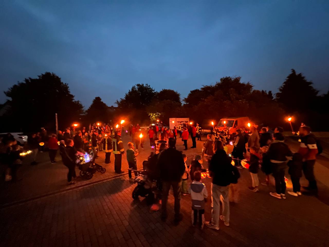 Kinder und Erwachsene mit Laternen sowie Feuerwehr mit Fackeln in der Abenddämmerung bei einem früheren Laternenlaufen