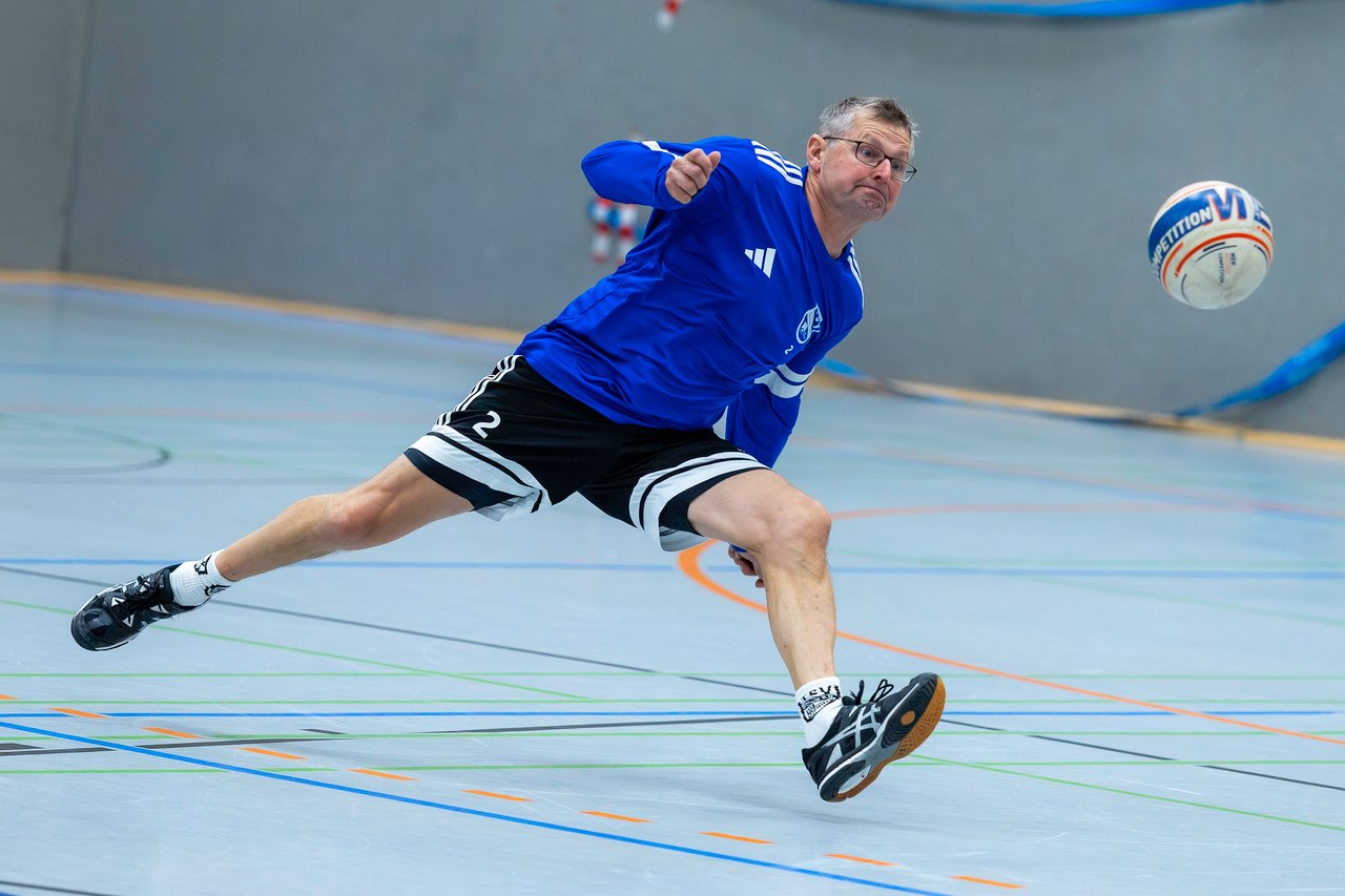 Ein Schülper Faustballspieler im blauen Trikot spielt den Ball im Sprung in der Sporthalle.