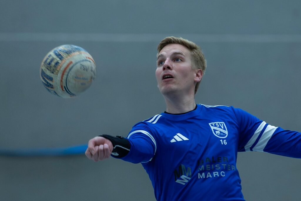 Ein Schülper Faustballspieler im blauen Trikot verfolgt den Ball mit ausgestrecktem Arm.